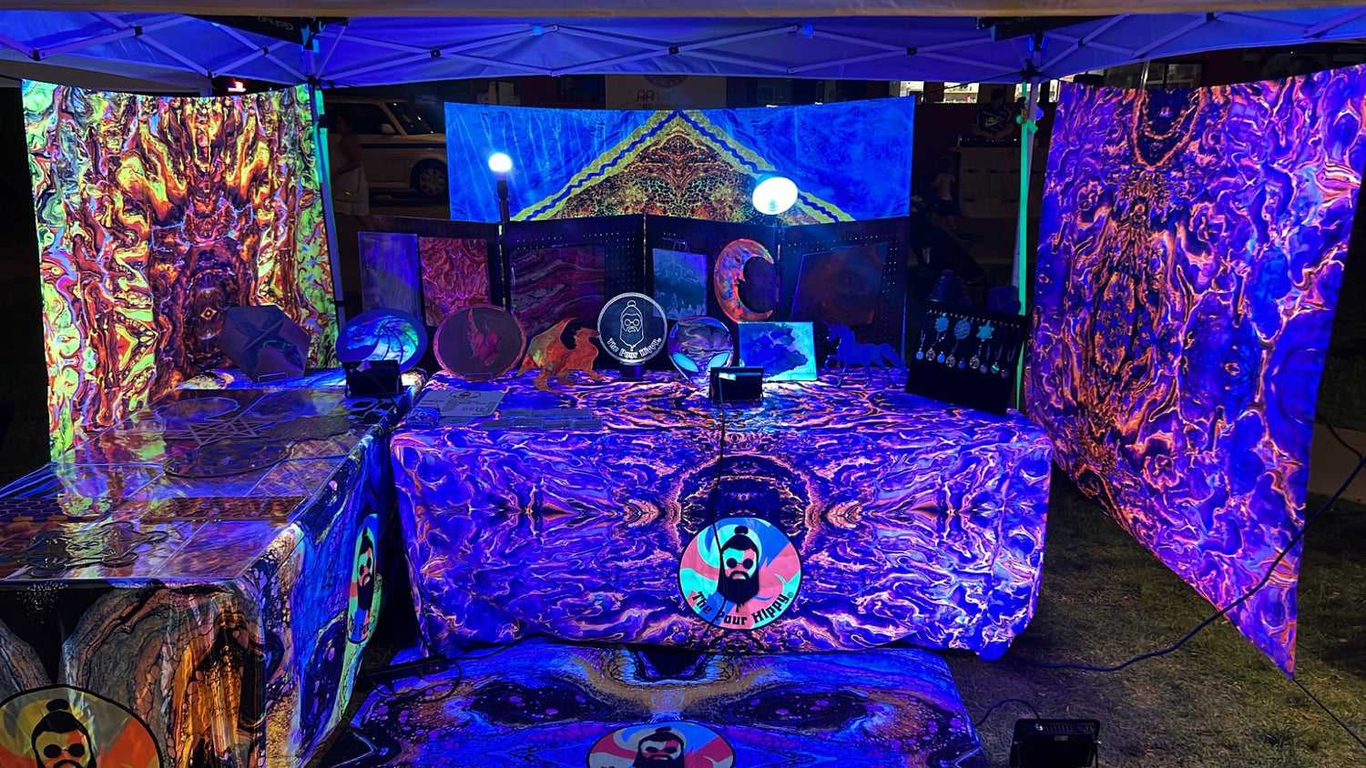 A glowing view of The Pour Hippy's event vending booth with paintings, tapestries, & posters